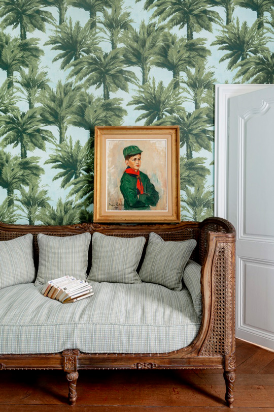 antic day bed covered with a velvet from Pierre Frey with a portrait of a boyscout and palm tree wallpaper from Maison Pierre Frey